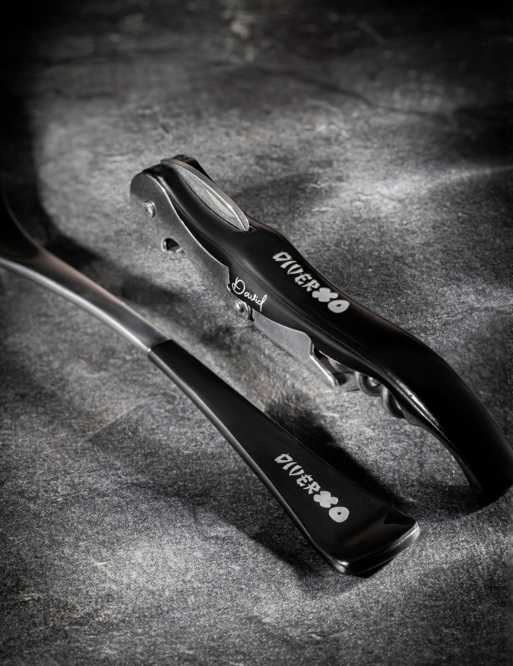 Black corkscrew and black top spoon with "DiverXO" restaurant logo engraved.