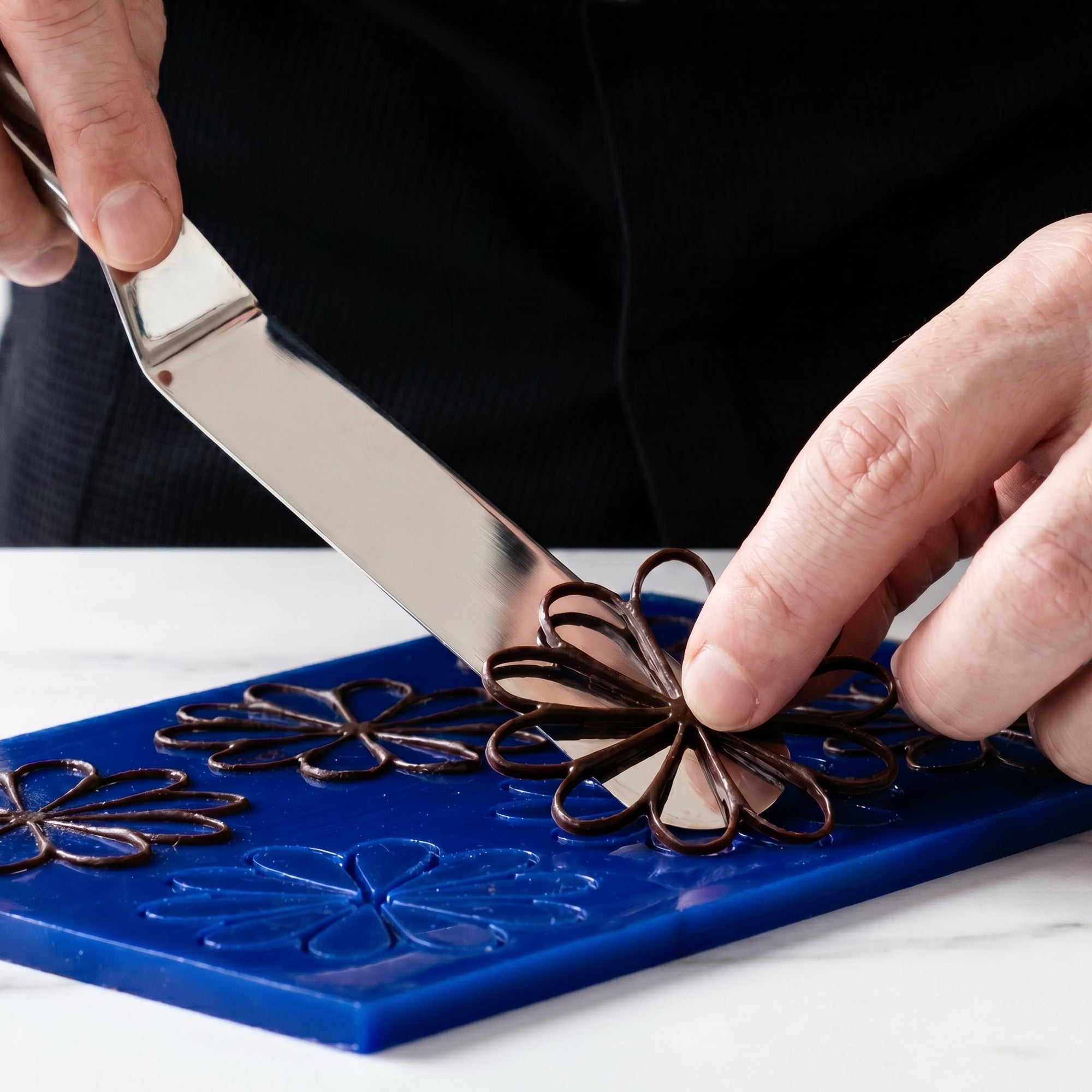 Chef carefully lifting a delicate sculpted chocolate garnish from a mould using a large stainless steel palette knife.